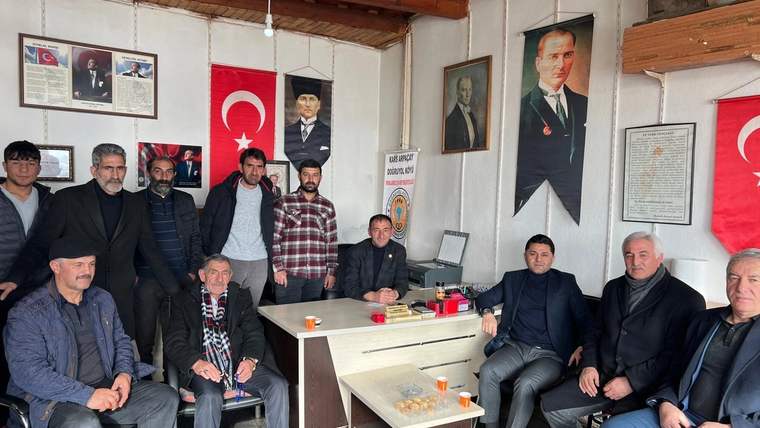 Türk bayrakları ve portrelerin bulunduğu odada, bir masa çevresinde oturan ve ayakta duran kişiler
