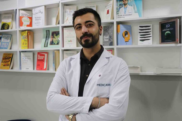 Üzerinde Medicana yazan beyaz önlüklü bir kişi, kitap ve broşürlerin bulunduğu rafların önünde duruyor.