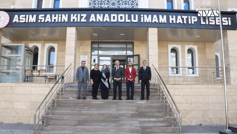 Bir grup insan, okul binasının önünde poz veriyor. Bina, açık renk taşlarla inşa edilmiş.