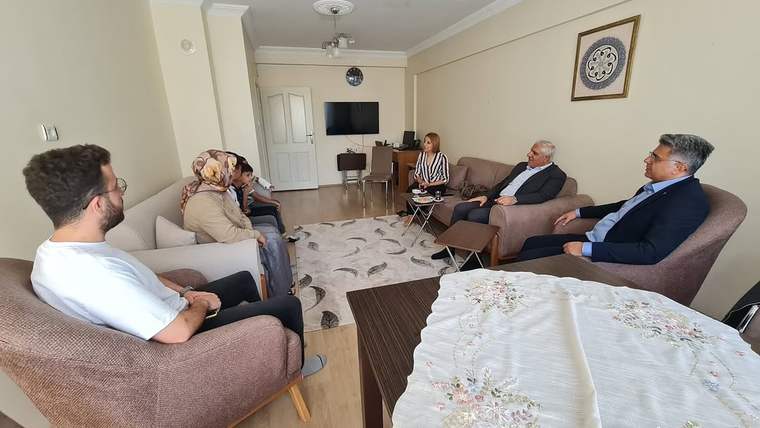 Bir oturma odasında koltuklara oturmuş, sohbet eden yedi kişi ve sehpa görülüyor.