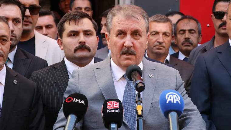Mikrofonun önünde konuşan bir kişi, arkasında kalabalık bir grup yer alıyor.