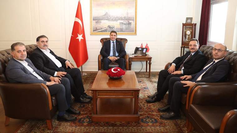 Türk bayrağının bulunduğu odada, sehpa çevresinde oturan altı erkek görülüyor.