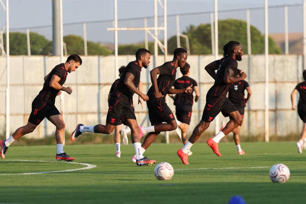 Antrenman sahasında siyah formalı futbolcular, toplarla birlikte koşu çalışması yapıyor.