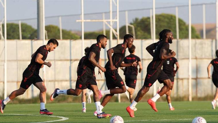 Antrenman sahasında siyah formalı futbolcular, toplarla birlikte koşu çalışması yapıyor.