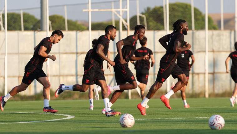 Antrenman sahasında siyah formalı futbolcular, toplarla birlikte koşu çalışması yapıyor.