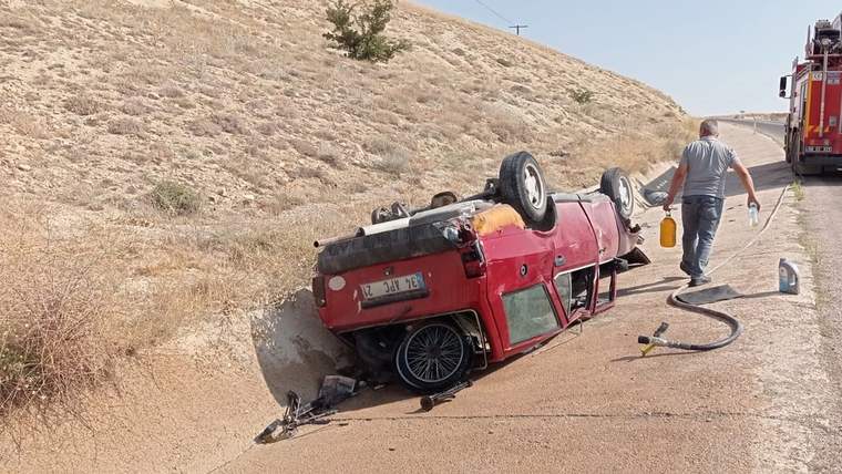 Yol kenarında ters dönmüş kırmızı bir otomobil, yanında hortum ve arkada duran itfaiye aracı görülüyor.