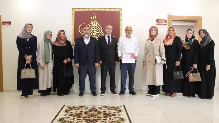 Bir grup kadın ve erkek, bir binanın içinde yan yana duruyor. Arkada büyük bir duvar resmi var.