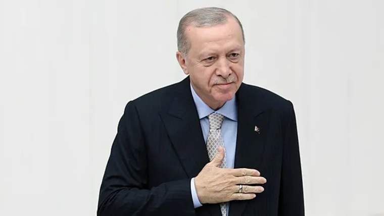 Kürsüde elini kalbine koymuş bir kişi, beyaz arka planda duruyor.