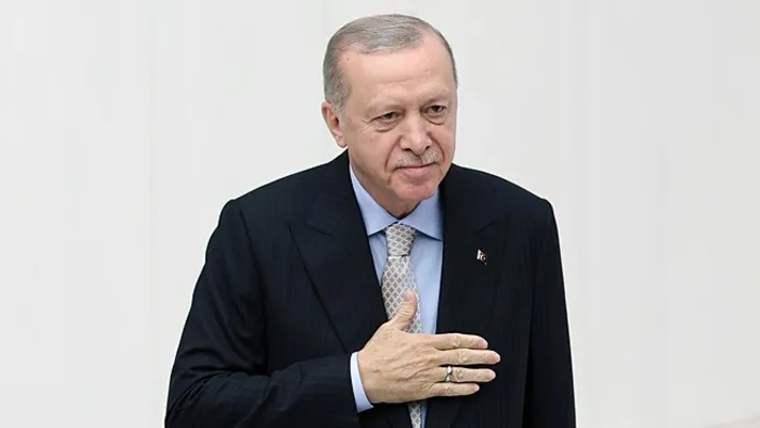 Kürsüde elini kalbine koymuş bir kişi, beyaz arka planda duruyor.