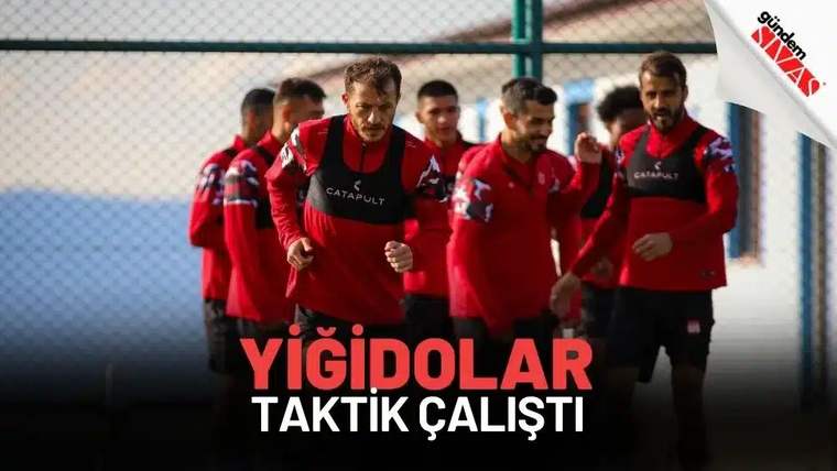 Kırmızı formalar giymiş futbolcular, antrenman sahasında taktik çalışması yapıyor.