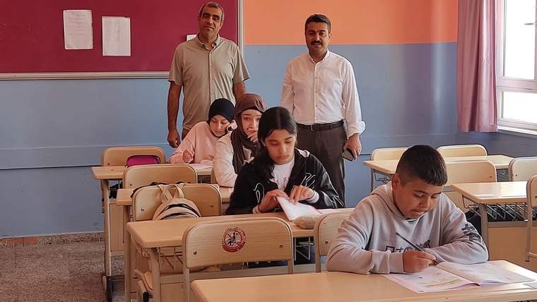 Sınıfta oturan öğrenciler, öğretmenlerin gözetiminde sınav provası yapıyor.
