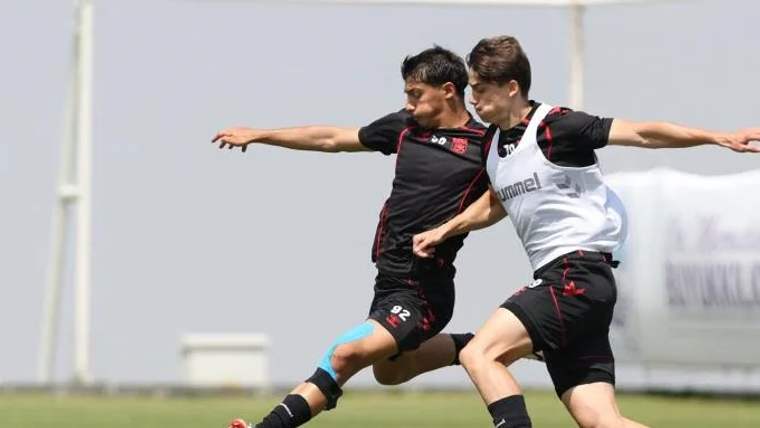 İki futbolcu, antrenman sırasında topa vurmak için mücadele ediyor.
