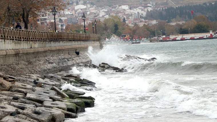 Dalgalı deniz, kayalık kıyı ve arka planda yerleşim alanı görünmekte.