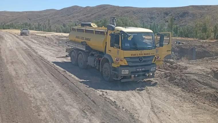 Sahada çalışan bir kamyon, toprak yolun yanında duruyor.