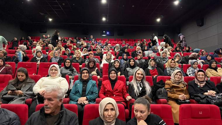 Kırmızı koltuklarda oturan kalabalık bir izleyici grubu, sinema salonunda film izliyor.