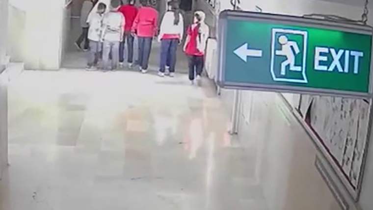 Bir grup öğrenci okul koridorunda yürürken, arka planda bir çıkış tabelası görünmektedir.