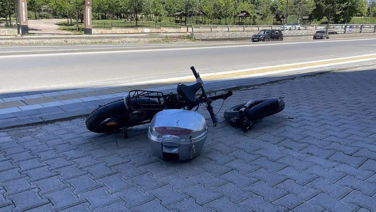 Yerde devrilmiş bir elektrikli bisiklet ve yanında bir kargo kutusu bulunuyor.