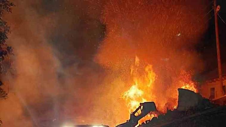 Gece karanlığında alevler içindeki yapının önünde iş makinesi ve hortum taşıyan bir kişi görülüyor.