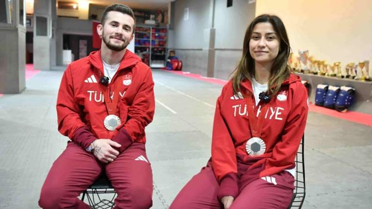 Gümüş madalya takan iki sporcu, spor salonunda oturuyor. Üzerlerinde Türkiye yazılı kıyafetler var.