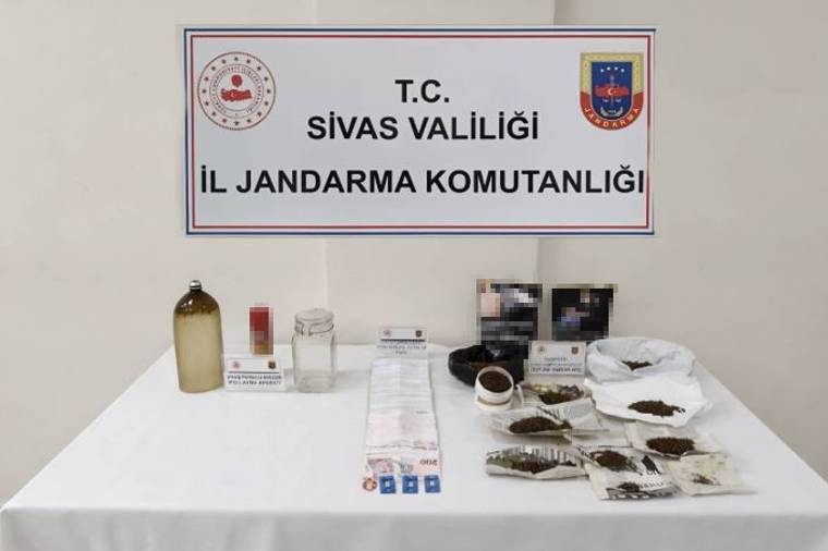 Masada çeşitli paketler, kavanoz ve şişeler; arkada Sivas Valiliği Jandarma Komutanlığı yazılı pano bulunuyor.