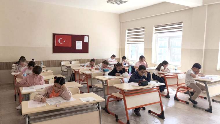 Sınıfta tekli sıralarda oturan öğrenciler, önlerindeki kâğıtlara yazı yazarak sınav oluyor.