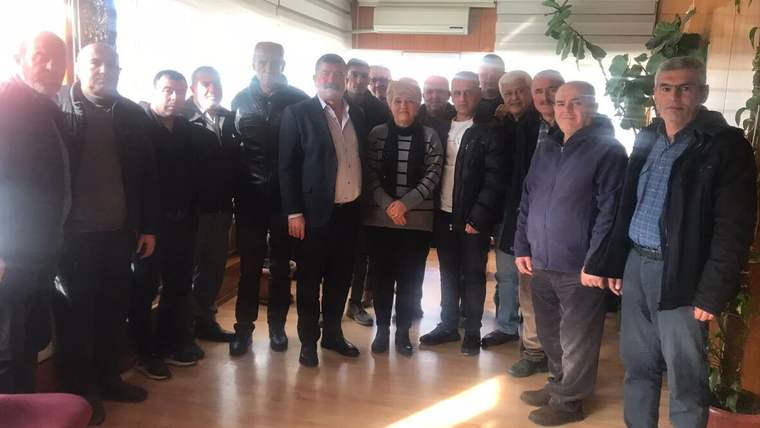 Ahşap zeminli bir salonda, farklı yaşlardan 14 kişi yan yana durarak kameraya bakıyor.