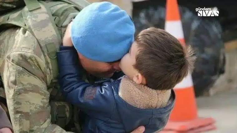 Asker üniforması giymiş bir kişi, bir çocuğun başını öpüyor.
