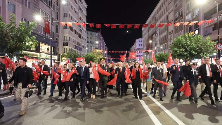 Gece aydınlatılan caddede Türk bayrakları taşıyan kalabalık, bando eşliğinde yürürken görülüyor.