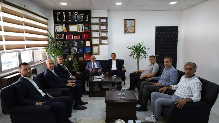 Bir ofiste koltuklarda oturan dokuz kişi, sehpa ve duvarındaki ödül vitrininin önünde poz veriyor.