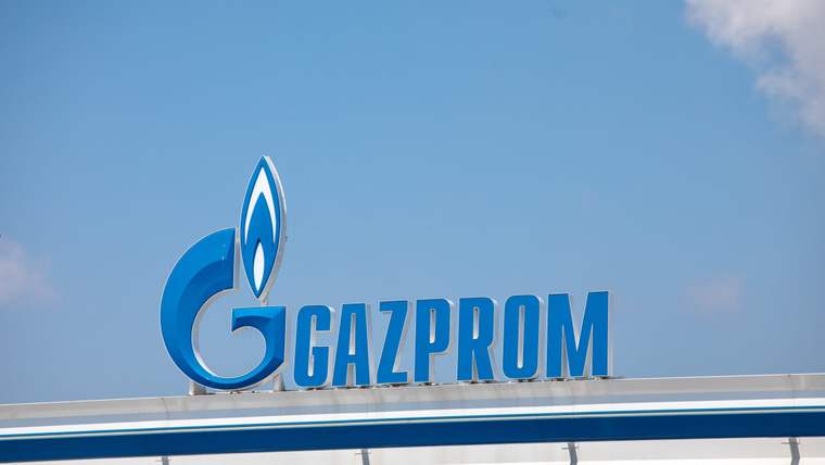 Mavi Gazprom logosu ve yazısı, mavi gökyüzü altında bir bina çatısının üzerinde görülüyor.