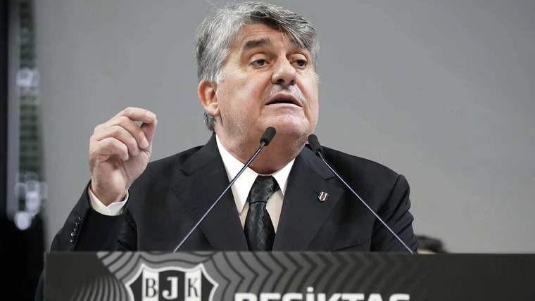 Mikrofon başında konuşan gri saçlı bir erkek, önündeki Beşiktaş logolu kürsüde elini kaldırıyor.