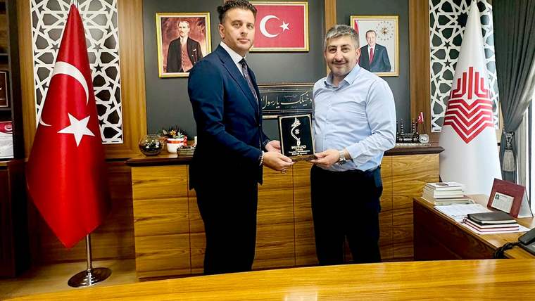 MÜSİAD temsilcisi ve Vakıflar Bölge Müdürü, bir plaket tutarak masanın önünde duruyor.
