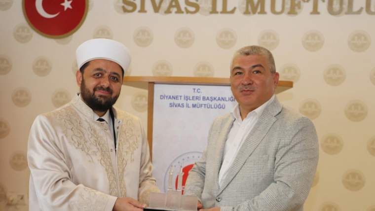 Diyanet İşleri Başkanlığı Sivas İl Müftülüğü yazılı panonun önünde iki kişi bir plaketi birlikte tutuyor.