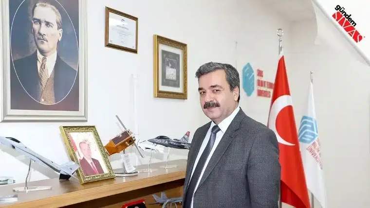 Bir adam, arkasında Atatürk'ün portresi ve Türk bayrağı ile bir masanın yanında duruyor.