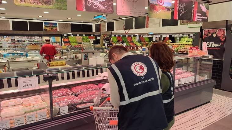 Süpermarkette et reyonunu inceleyen, üzerinde Ticaret Bakanlığı yazılı yelek giyen iki kişi görülüyor.