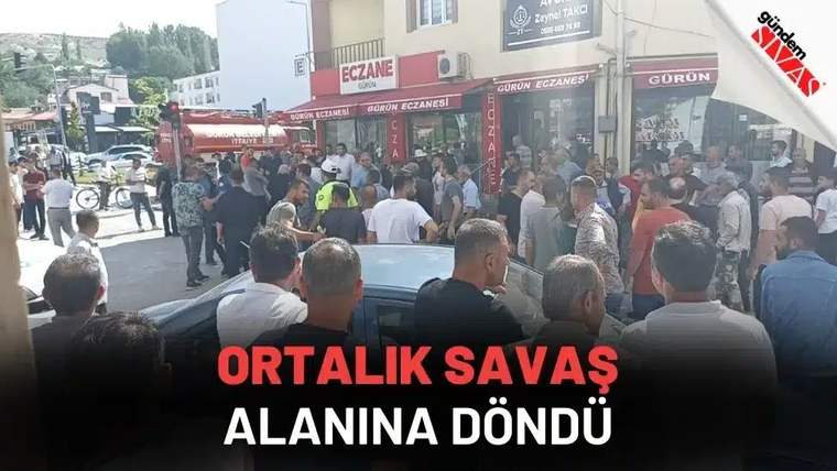 Eczane tabelalarının bulunduğu cadde üzerinde çok sayıda kişi, park halindeki bir otomobilin çevresinde toplanıyor.