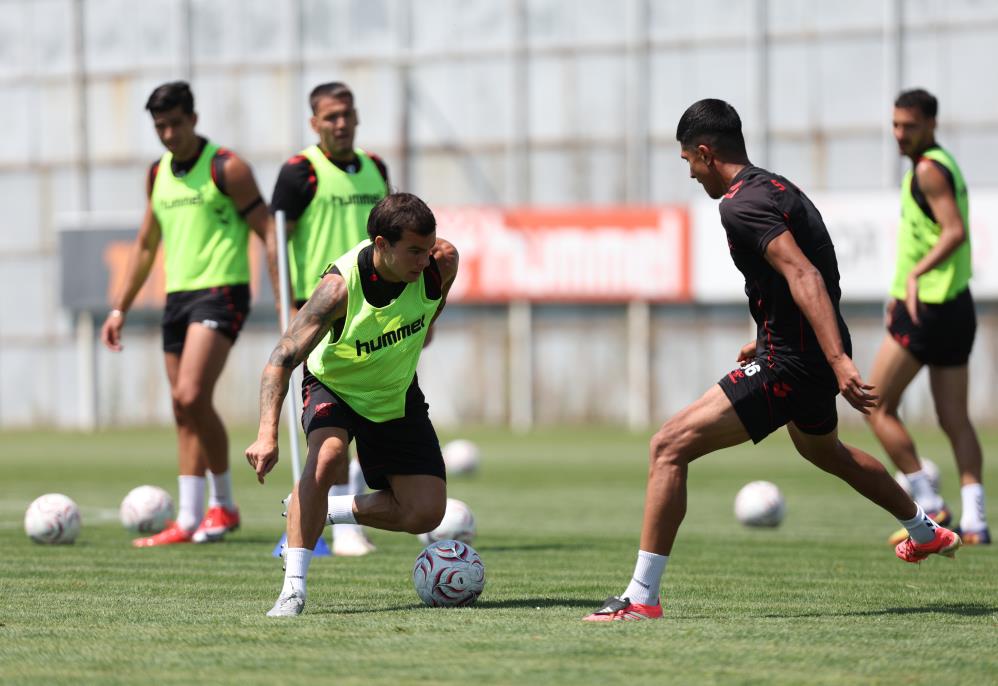 Antrenman sahasında futbolcular, yeşil yelek giymiş iki oyuncu top kapma çalışması yapıyor.