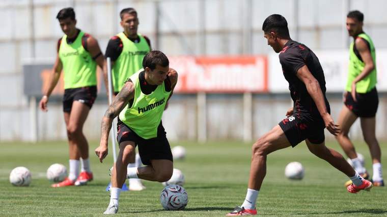 Antrenman sahasında futbolcular, yeşil yelek giymiş iki oyuncu top kapma çalışması yapıyor.