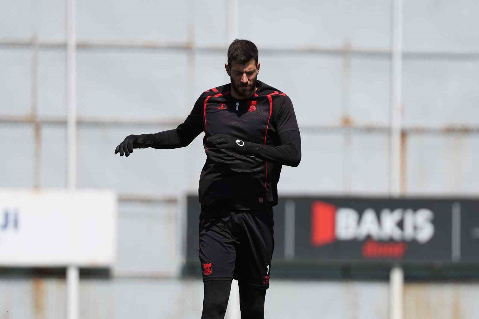 Antrenman yapan bir futbolcu, siyah antrenman kıyafeti giymekte ve eldiven takmakta.