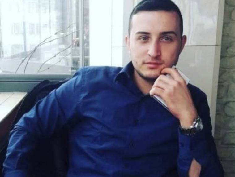 Koyu mavi gömlek giyen bir erkek, pencere önünde otururken elini çenesine dayamış.