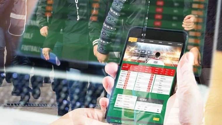 Bir kişinin elinde cep telefonu, ekranda bahis uygulaması açık.