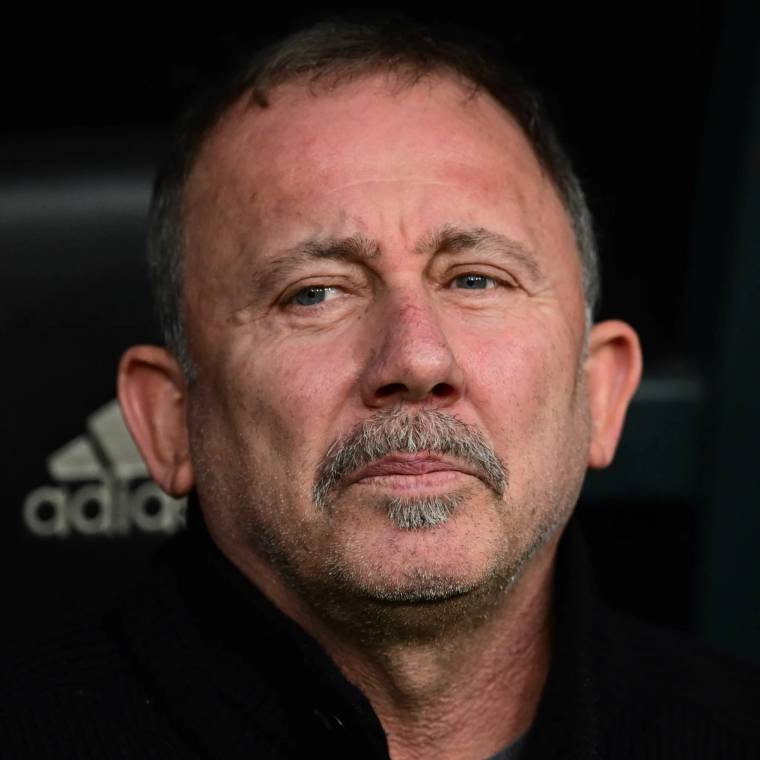 Yakın planda, kısa saçlı ve kirli sakallı bir adamın yüzü; arka planda Adidas logosunun bir bölümü görülüyor.