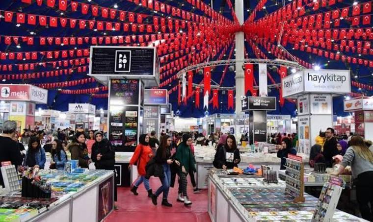 Türk bayraklarıyla süslenmiş kitap fuarında stantlar arasında dolaşan ziyaretçiler görülüyor.