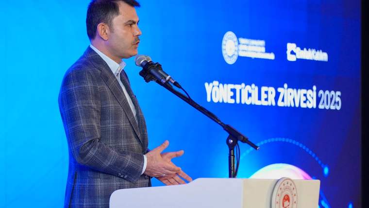 Mikrofonun önünde konuşan bir kişi, arka planda etkinlik logosu ve yazılar görünmekte.