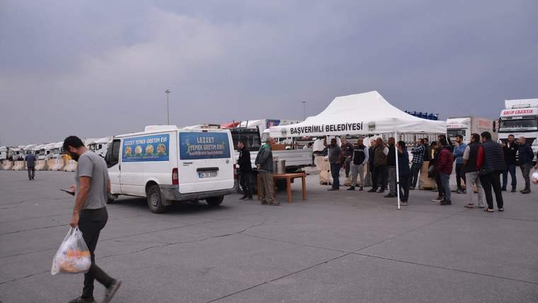 Üzerinde Başverimli Belediyesi yazan çadırın önünde sırada bekleyen insanlar ve park halindeki minibüsler görülüyor.