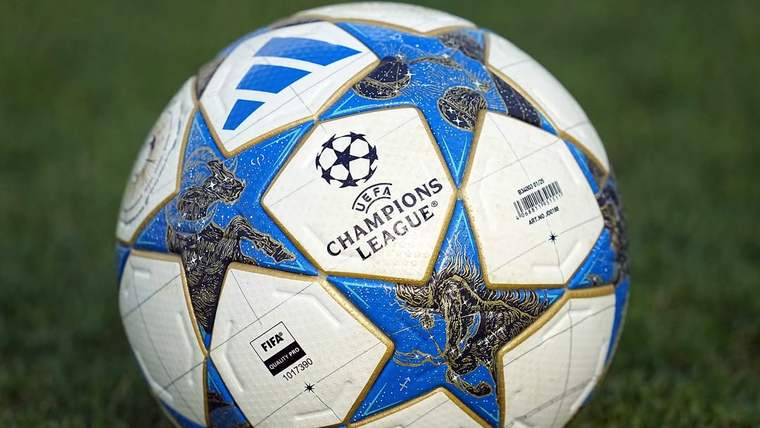 Çim zemin üzerinde, UEFA Şampiyonlar Ligi logolu beyaz ve mavi futbol topu yakın planda duruyor.