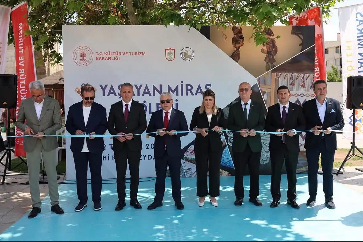 Sekiz kişi, üzerinde “Yaşayan Miras” yazılı pankart önünde kurdele keserken yan yana duruyor.