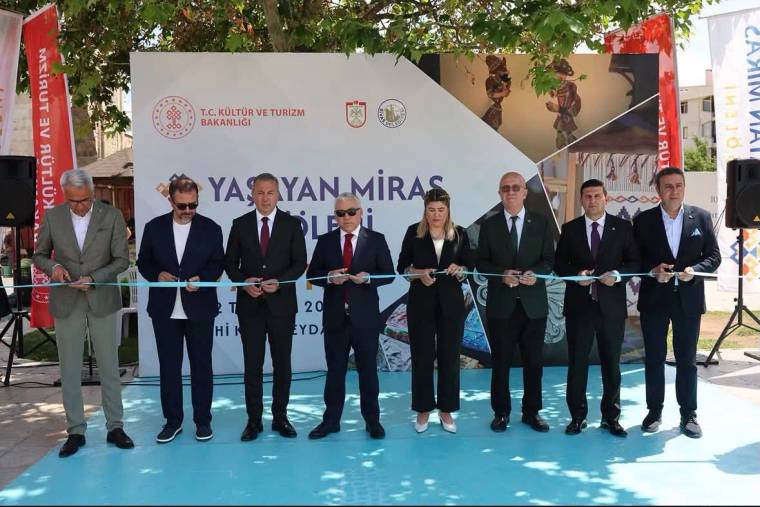 Sekiz kişi, üzerinde “Yaşayan Miras” yazılı pankart önünde kurdele keserken yan yana duruyor.
