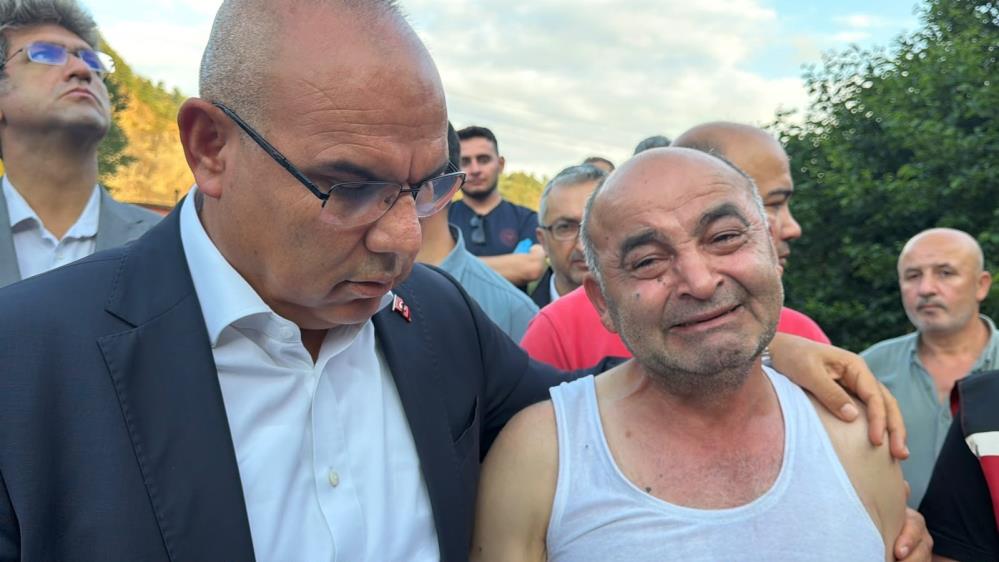 Kalabalık arasında bir adam gözyaşlarıyla dururken, yanındaki takım elbiseli kişi elini omzuna koyuyor.