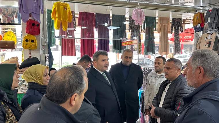 Giyim mağazasında askılı kıyafetlerin arasında duran bir grup yetişkin, birlikte konuşuyor.